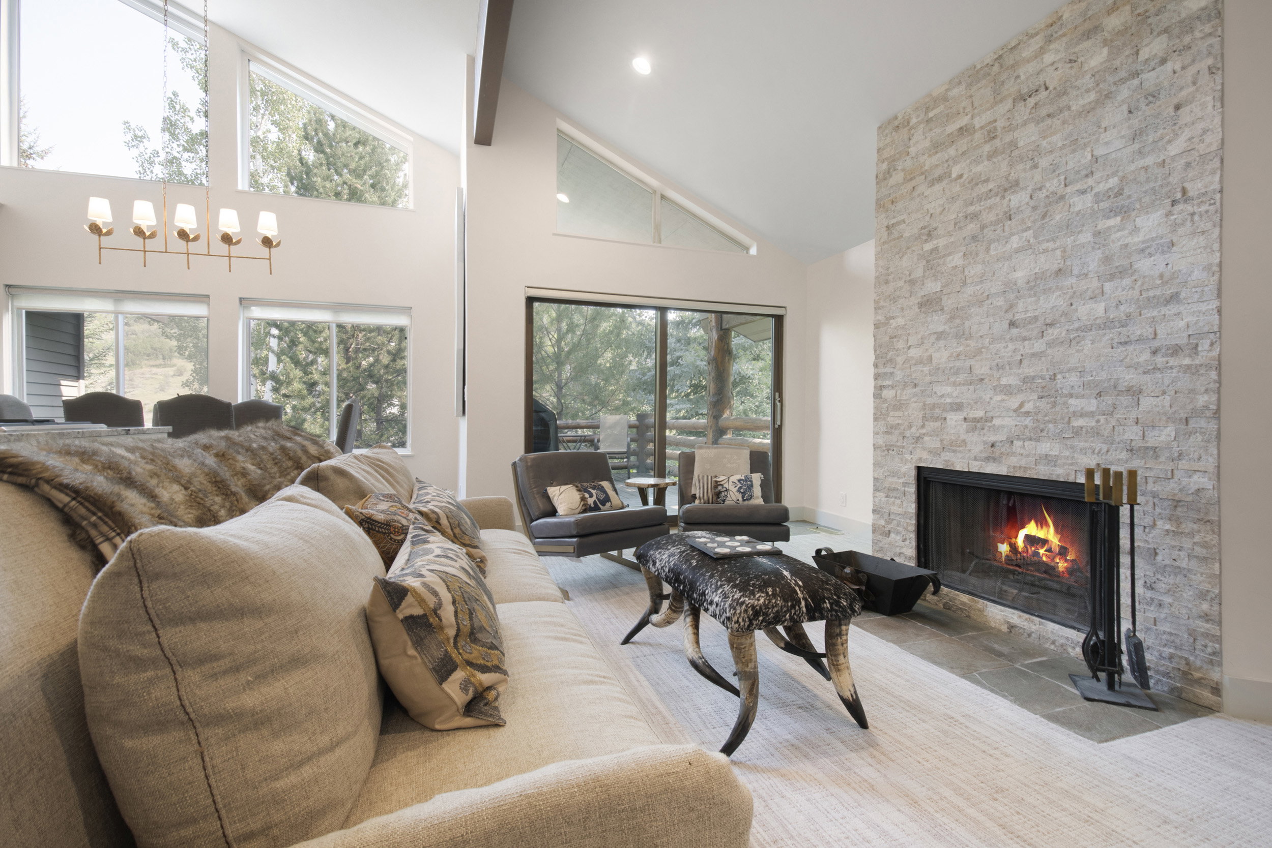 Vaulted ceiling living area featuring a stacked stone fireplace with a black metal firebox, large glass sliding doors, and ample natural light from multiple windows