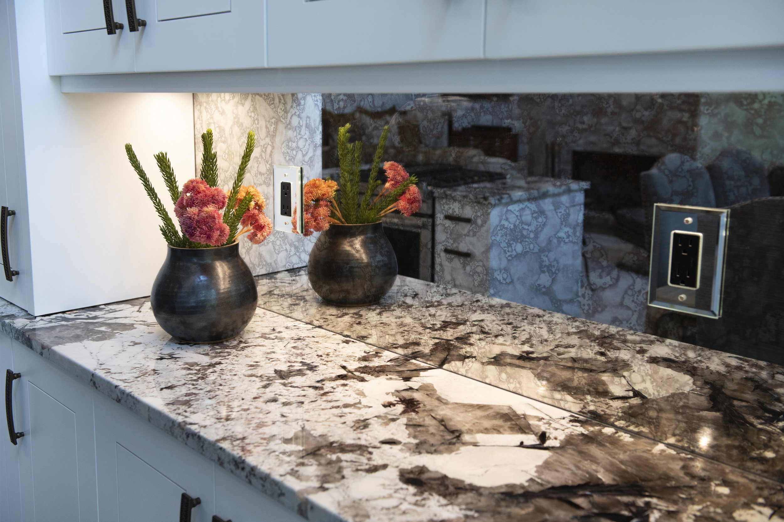 Contemporary kitchen featuring under-cabinet lighting, sleek white cabinetry with dark hardware, and a striking patterned countertop