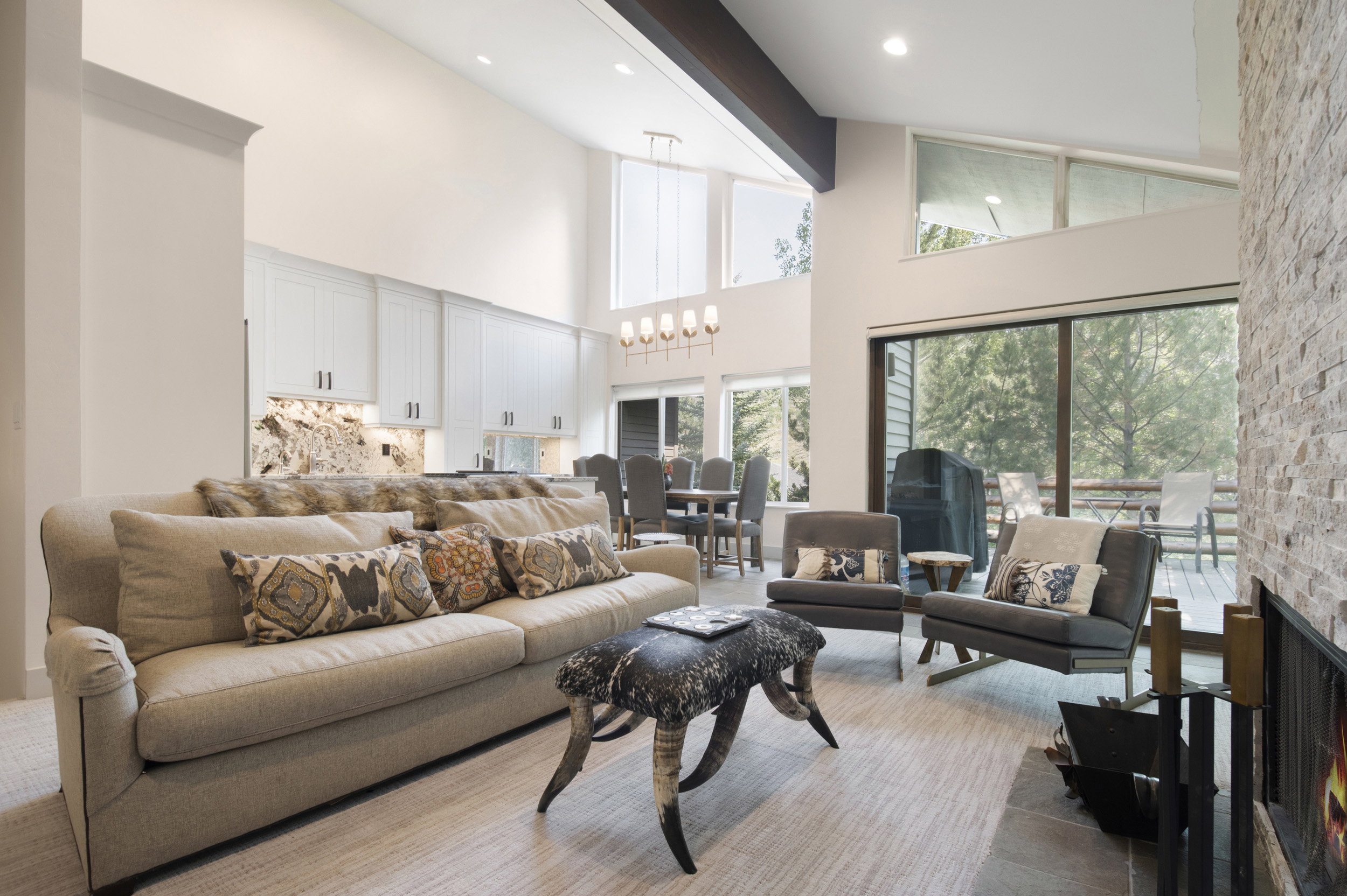 Open-concept living space featuring high vaulted ceilings, a stone-clad fireplace, and large sliding glass doors leading to an exterior deck