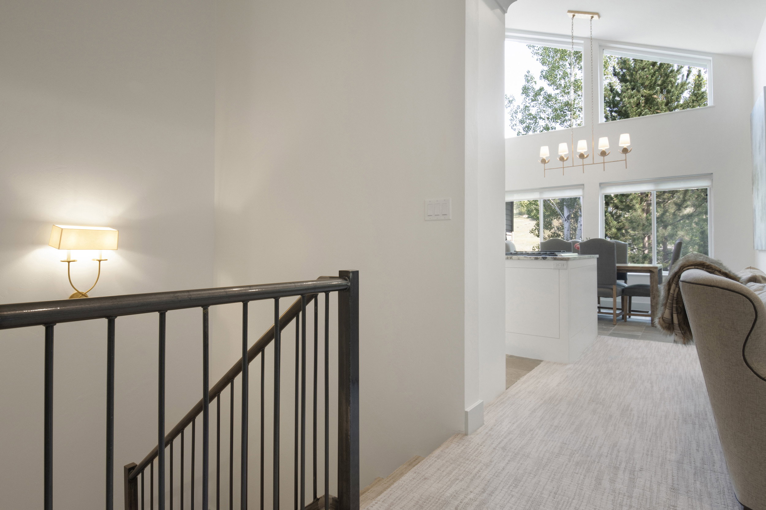 Open-concept living space with vaulted ceilings, large picture windows, a contemporary chandelier, and a stairway featuring a wrought iron railing with a wall sconce