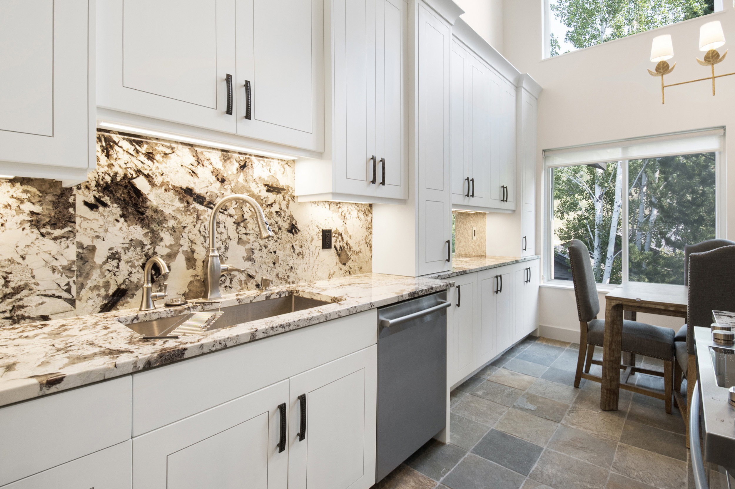 Kitchen featuring white cabinetry with dark hardware, stone countertops and backsplash, an undermount sink with a gooseneck faucet, and slate-style flooring