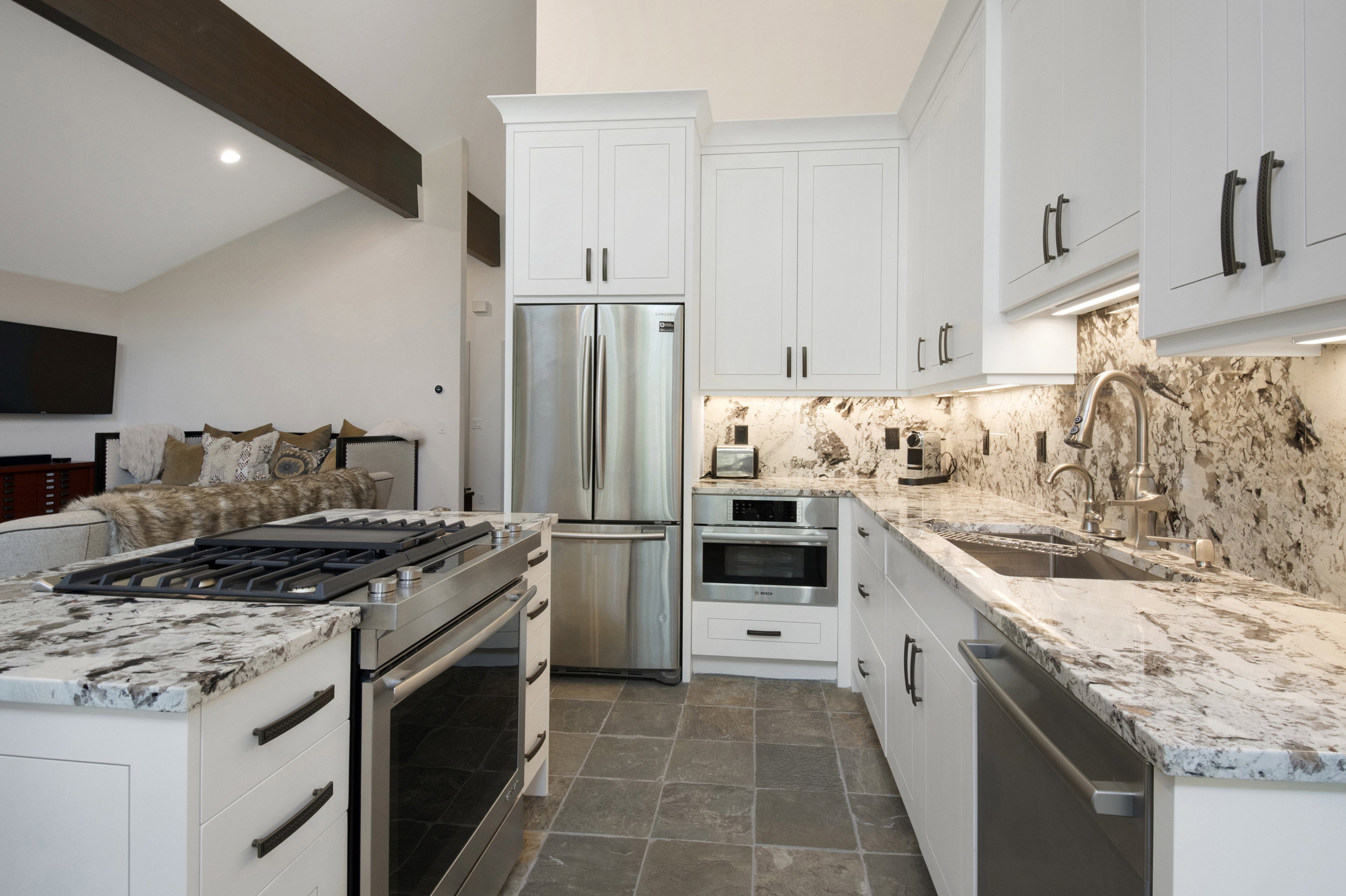 Gourmet kitchen featuring white shaker cabinetry, stainless steel appliances, premium stone countertops, a coordinating stone backsplash, and slate-finish flooring
