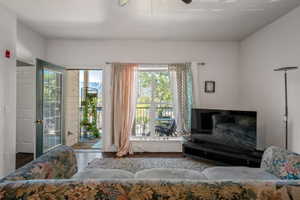 Living area with dark wood-finish flooring, white walls, a ceiling fan, and a glass-paneled door opening to a balcony