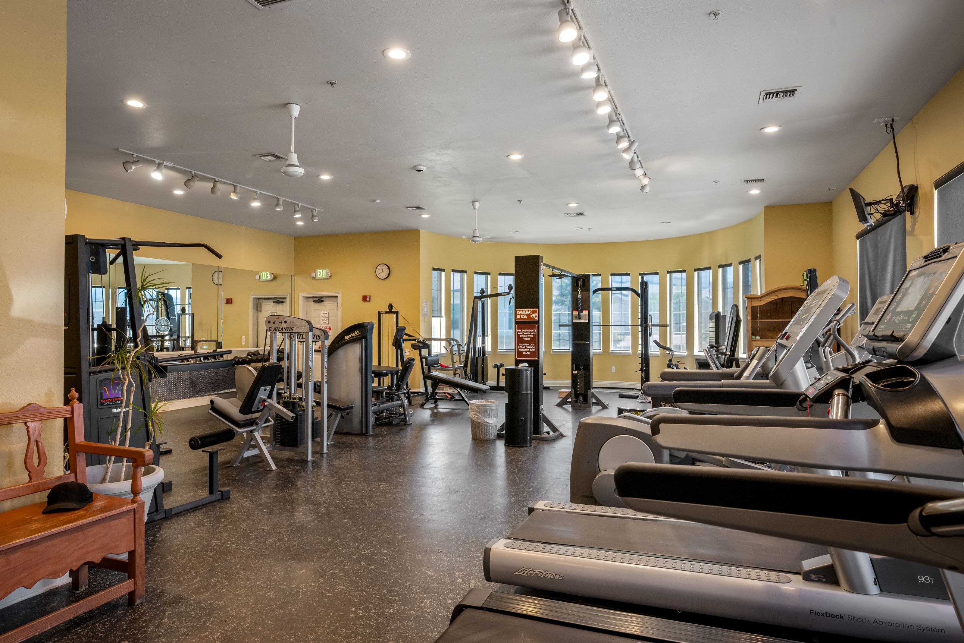 Fitness center featuring multiple treadmills, strength training equipment, track lighting, and a curved window wall