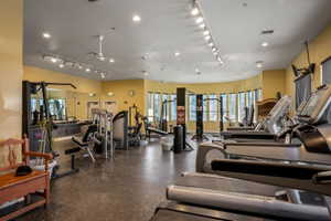 Fitness center featuring multiple treadmills, strength training equipment, track lighting, and a curved window wall
