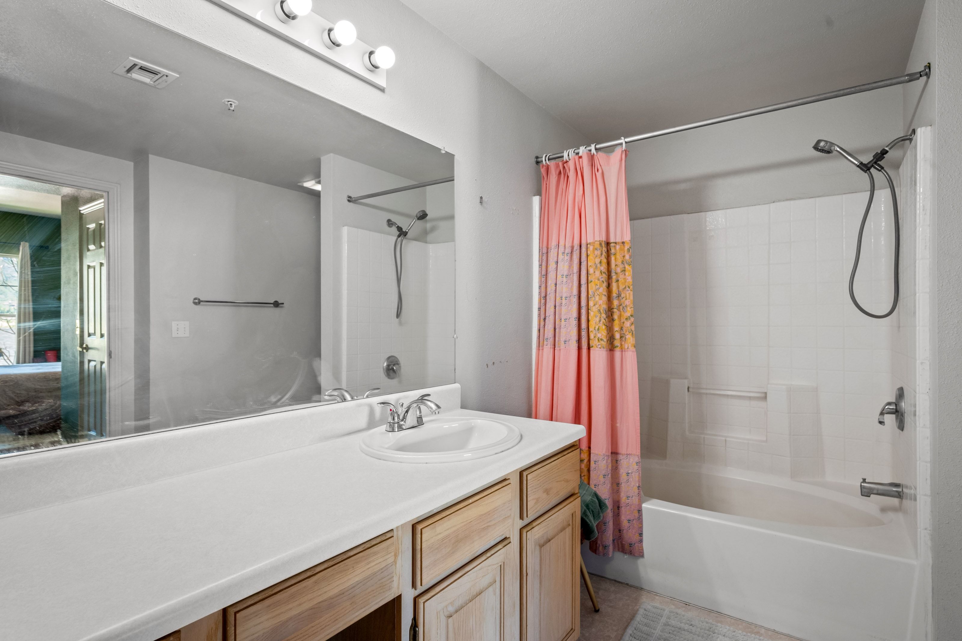 Bathroom featuring a single vanity with a white countertop, wood-finish cabinetry, an integrated sink, a large mirror, and a shower-bathtub combination with white subway tile surround