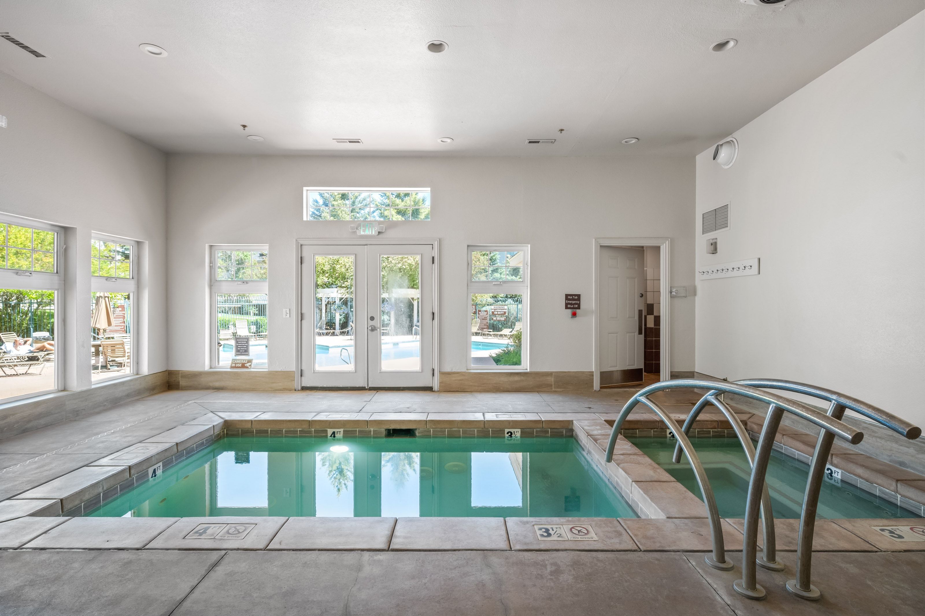Indoor aquatic area featuring two integrated spas with metal railings, a light-colored tile surround, and expansive windows