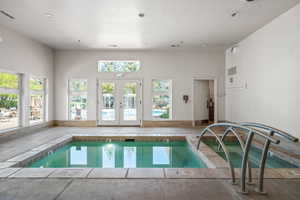 Indoor aquatic area featuring two integrated spas with metal railings, a light-colored tile surround, and expansive windows