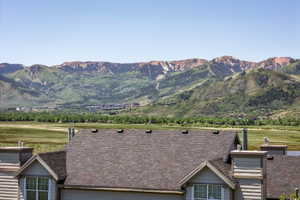 Mountain landscape with expansive green valleys and distant treeline, framed by a residential roofline featuring multiple chimneys and gabled dormers