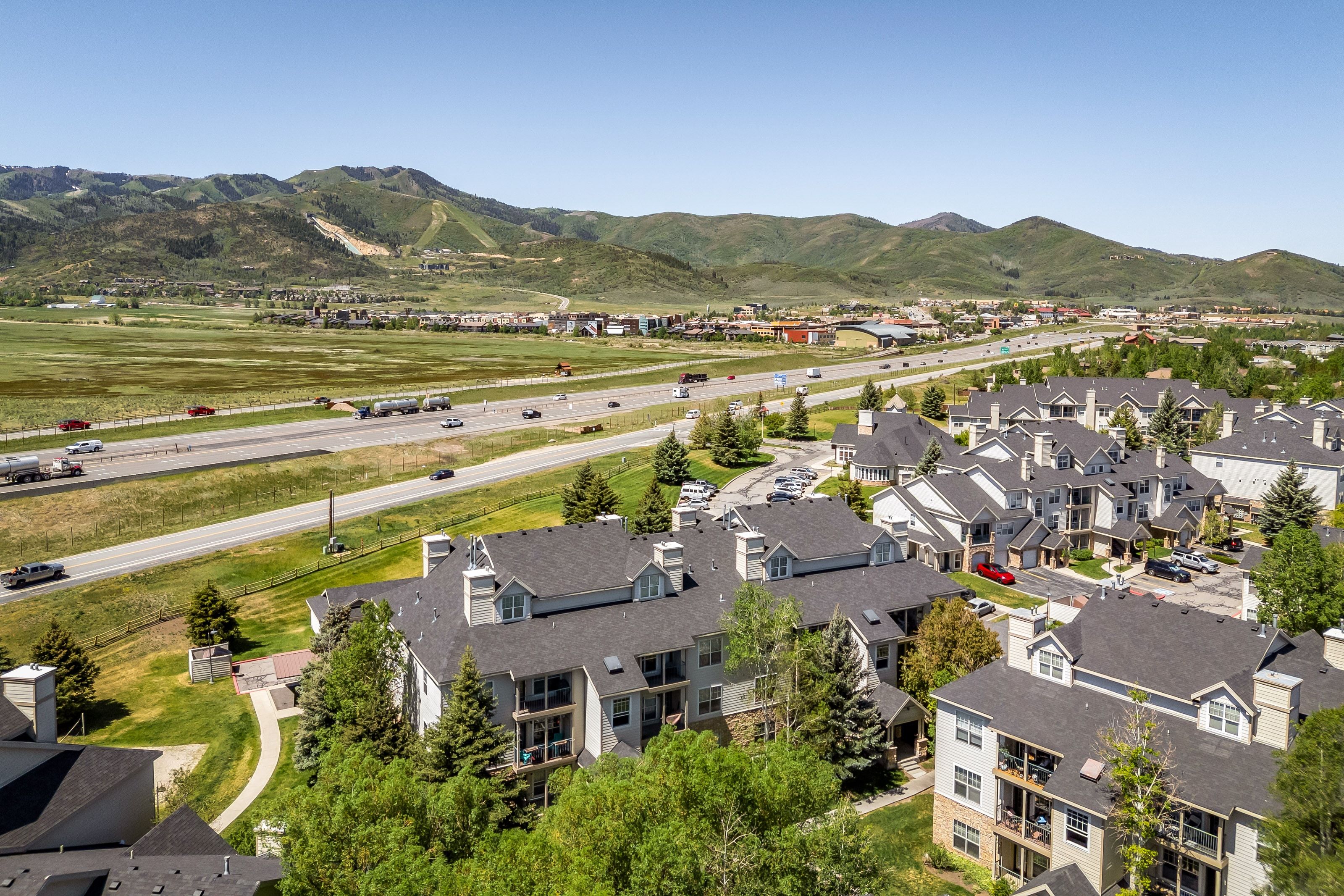 Aerial perspective showcasing multi-story residential buildings with dark shingled roofs and dormer windows, surrounded by green landscaping and mature trees
