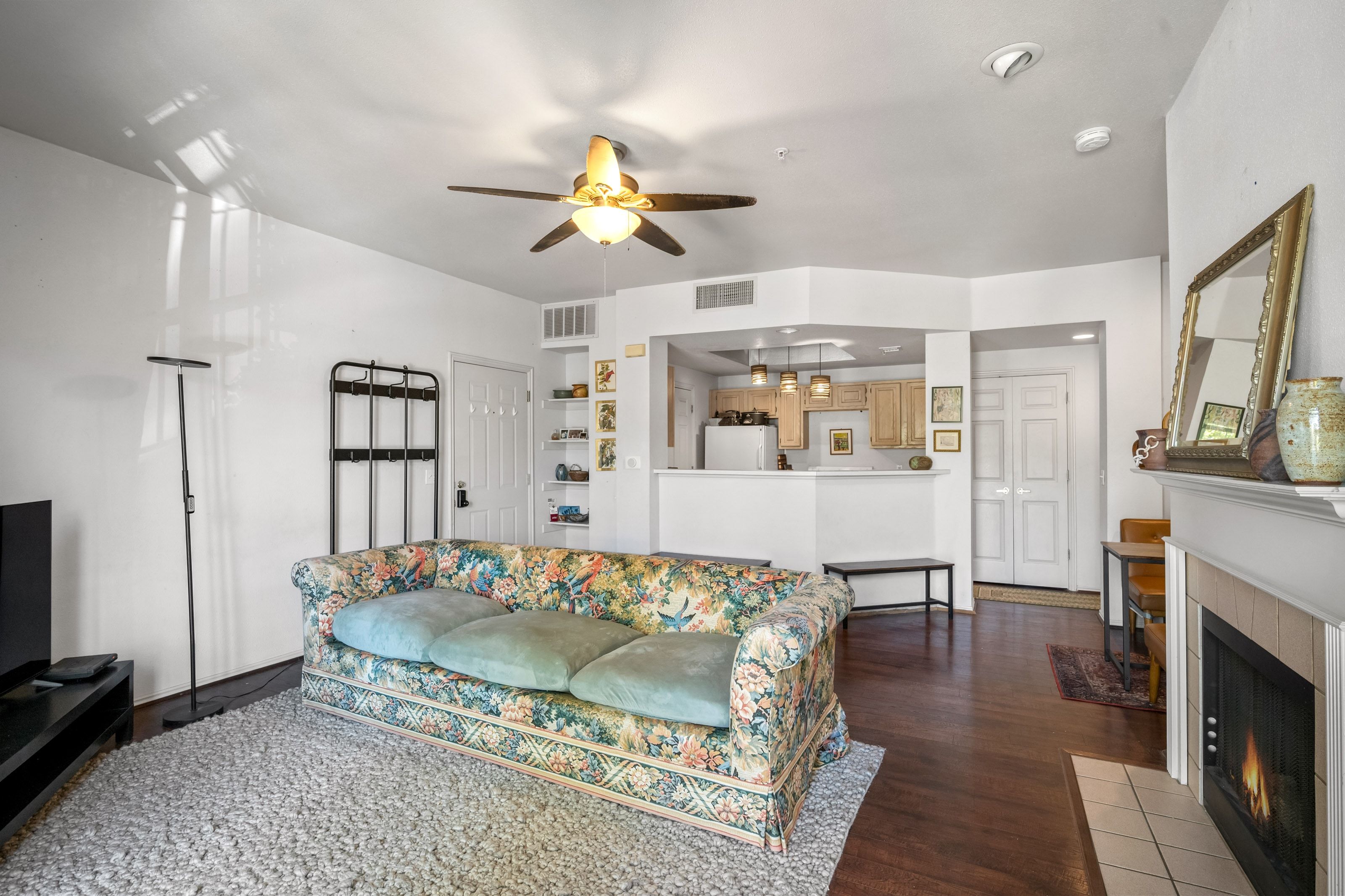 Open-concept living space featuring wood-finish flooring, a ceiling fan with integrated lighting, and a built-in fireplace with a tiled surround