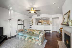 Open-concept living space featuring wood-finish flooring, a ceiling fan with integrated lighting, and a built-in fireplace with a tiled surround