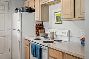 Kitchen featuring light wood cabinetry, white countertops, and a white electric range
