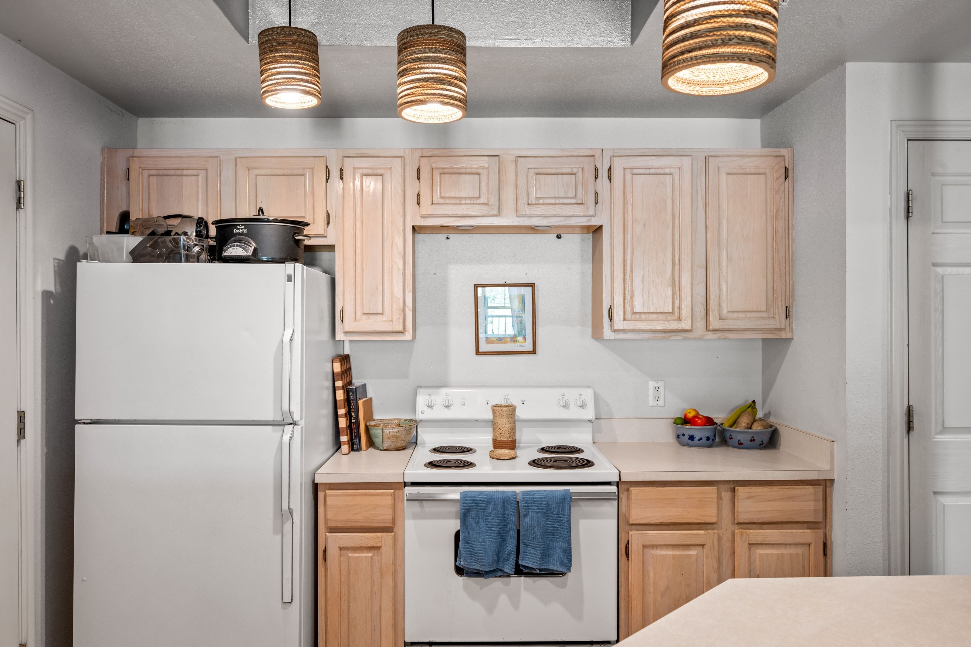 Kitchen area featuring wood-finish cabinetry, white appliances, and pendant lighting fixtures