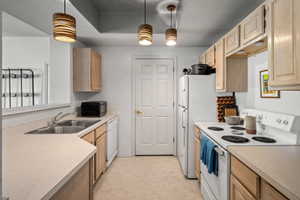 Kitchen featuring light-tone wood cabinetry, laminate countertops, a double basin stainless steel sink, white appliances, and pendant lighting