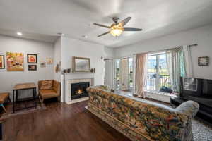 Living area featuring wood-finish flooring, a fireplace with a white mantel and tile surround, and a ceiling fan with integrated lighting
