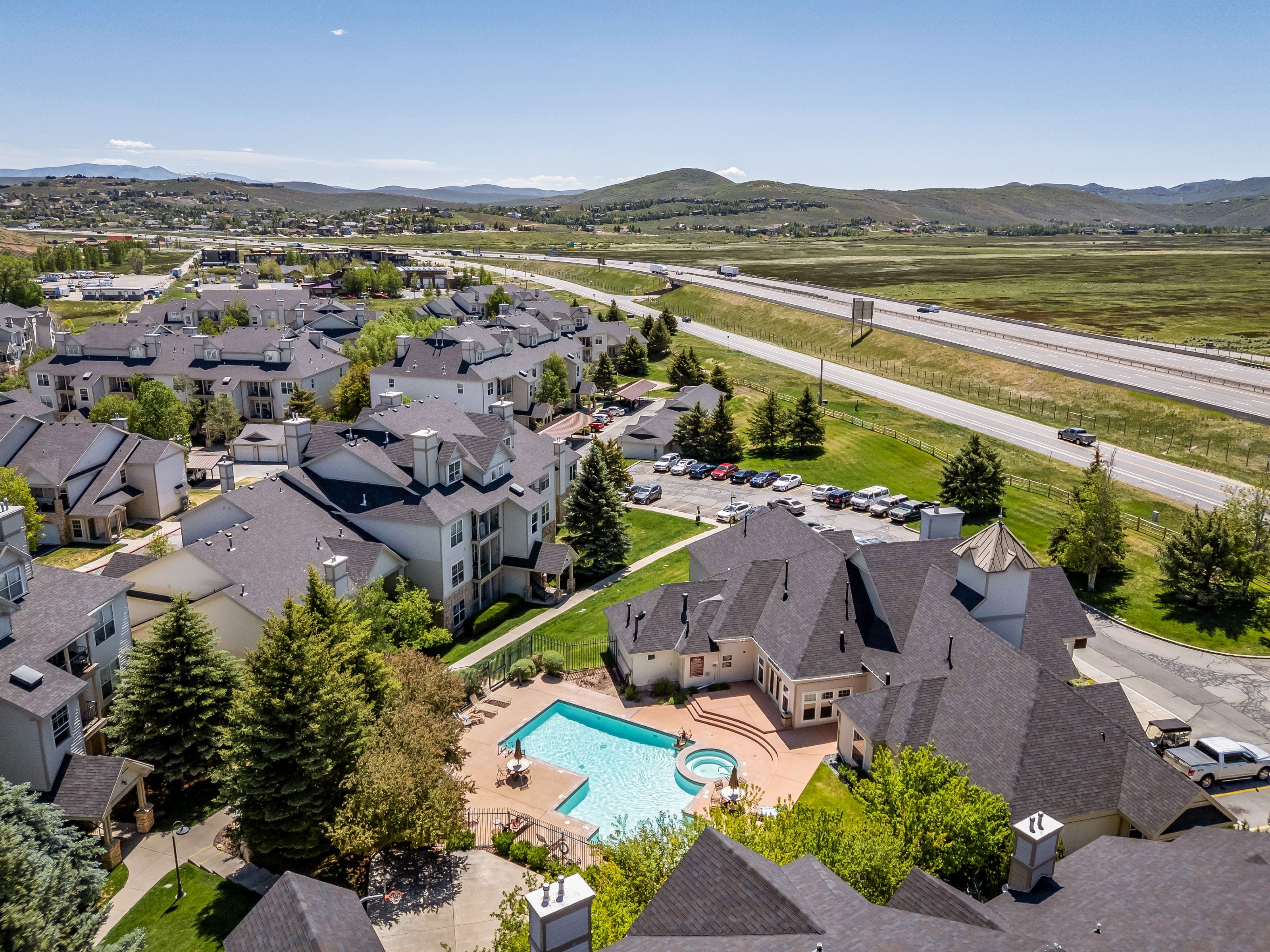 Expansive community featuring multiple residential buildings with dark shingle roofs, a central swimming pool with an integrated spa, and surrounding green spaces