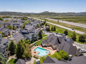 Expansive community featuring multiple residential buildings with dark shingle roofs, a central swimming pool with an integrated spa, and surrounding green spaces