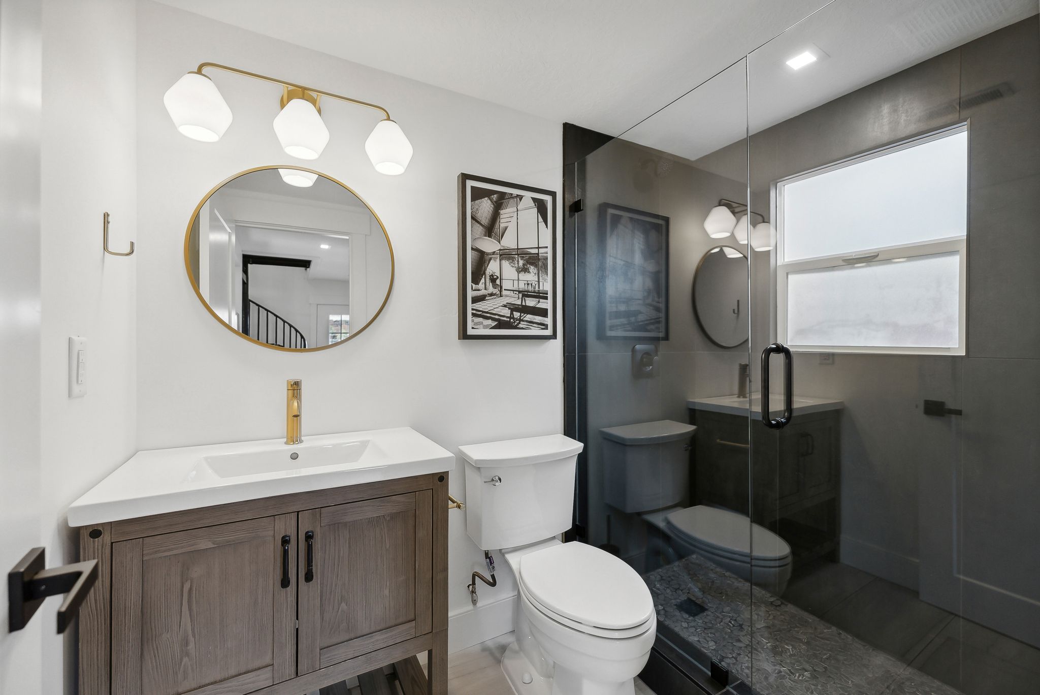 Bathroom featuring a wood-finish vanity with an integrated sink and gold-finish faucet, framed by a round gold-finish mirror and a three-light vanity fixture