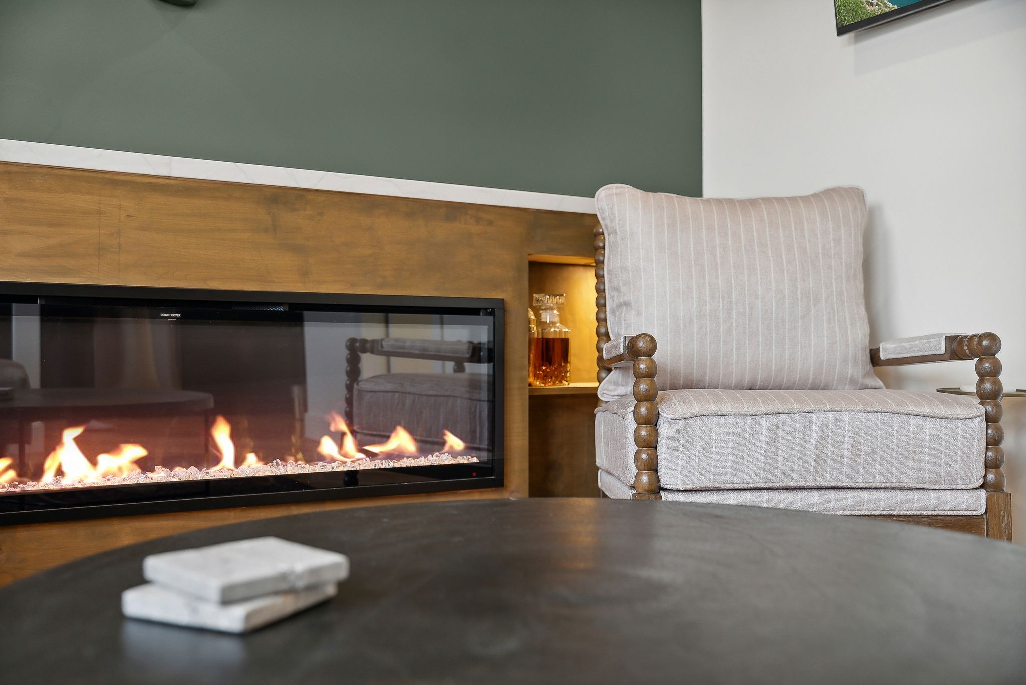 Built-in linear fireplace with glass enclosure, integrated into a wood-finish wall structure featuring an illuminated display niche