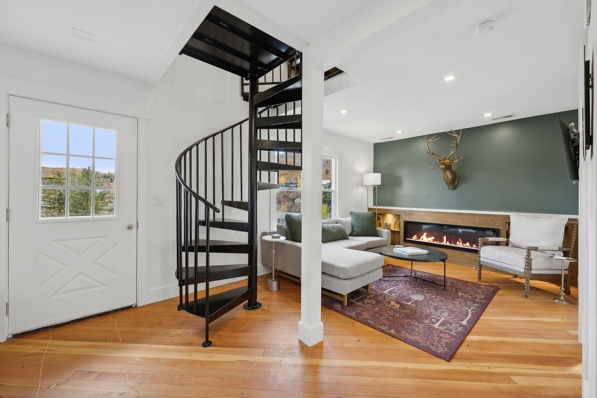 Hardwood flooring highlights an open living area featuring a sleek linear fireplace with a wood-finish mantel and a contrasting accent wall