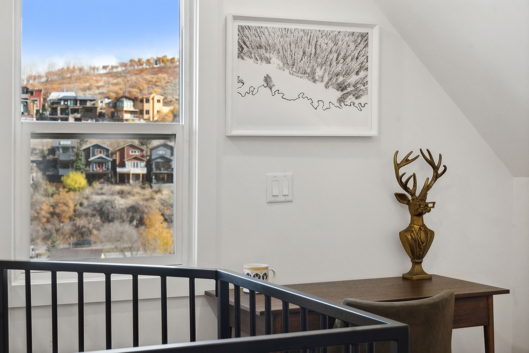 White framed window overlooking a hillside with residential structures and natural foliage