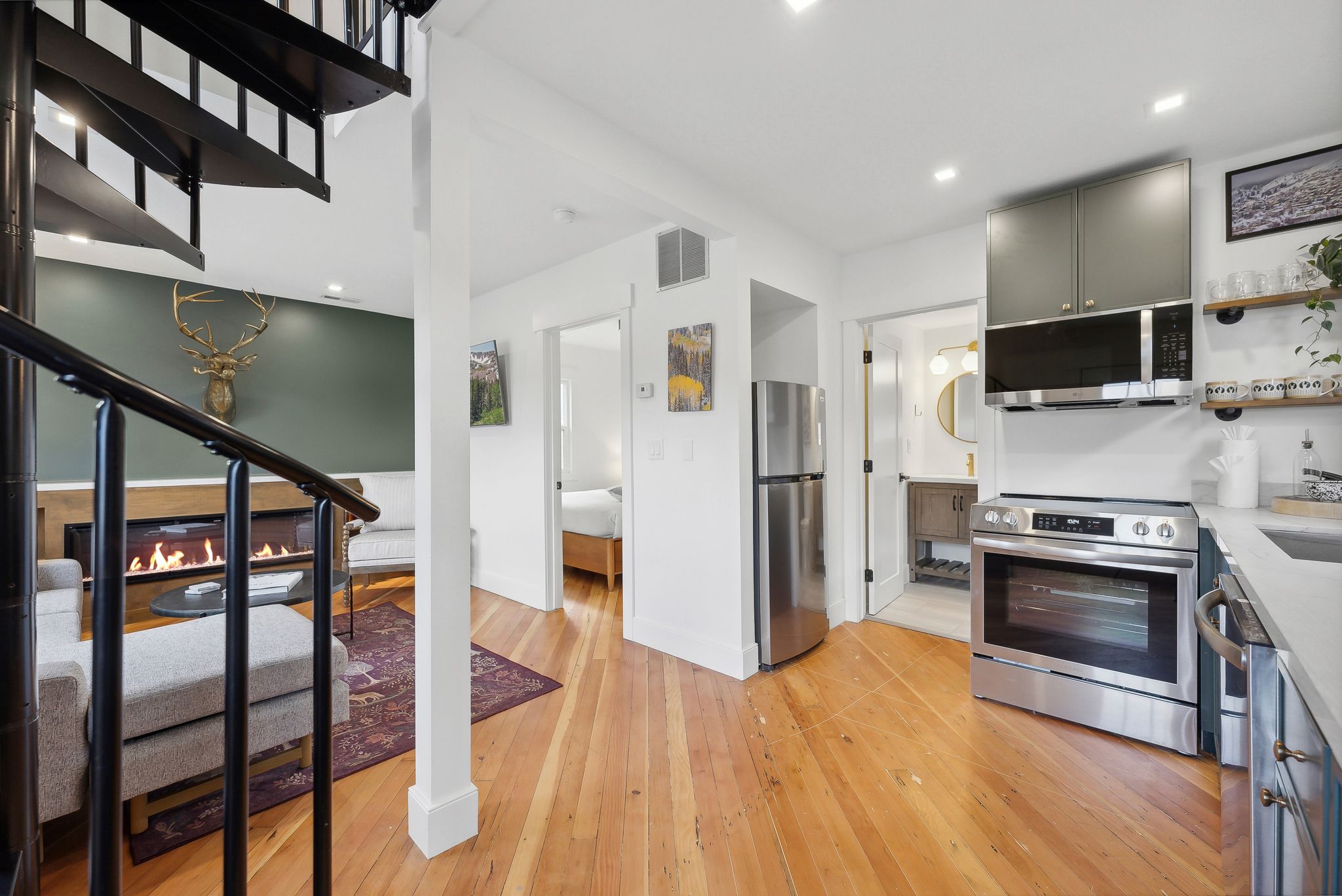 Open-concept living space featuring wood-finish flooring, a modern kitchen with stainless steel appliances, a built-in fireplace, and a black spiral staircase