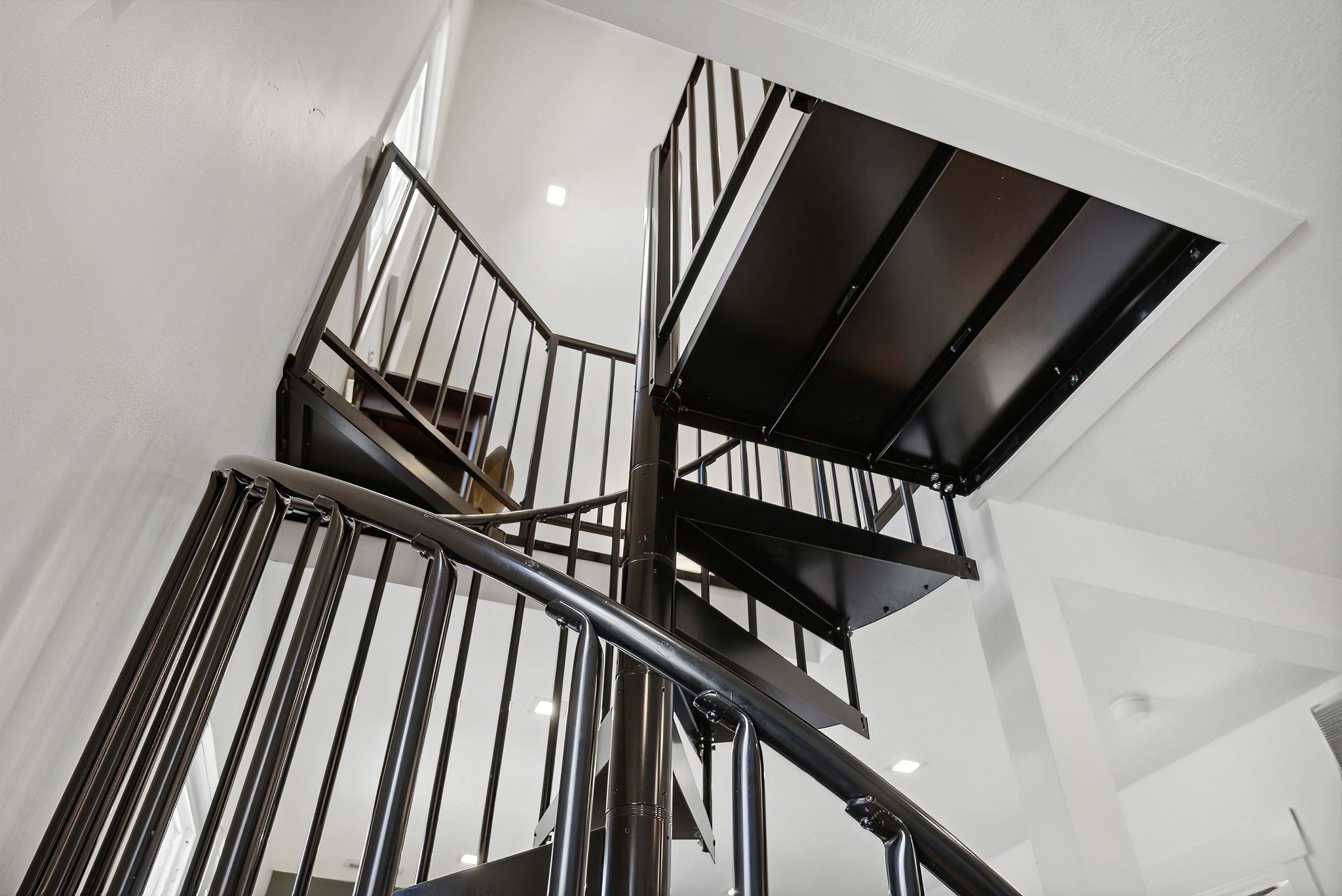 Spiral staircase featuring black metal construction, white wall finishes, recessed lighting, and a prominent window