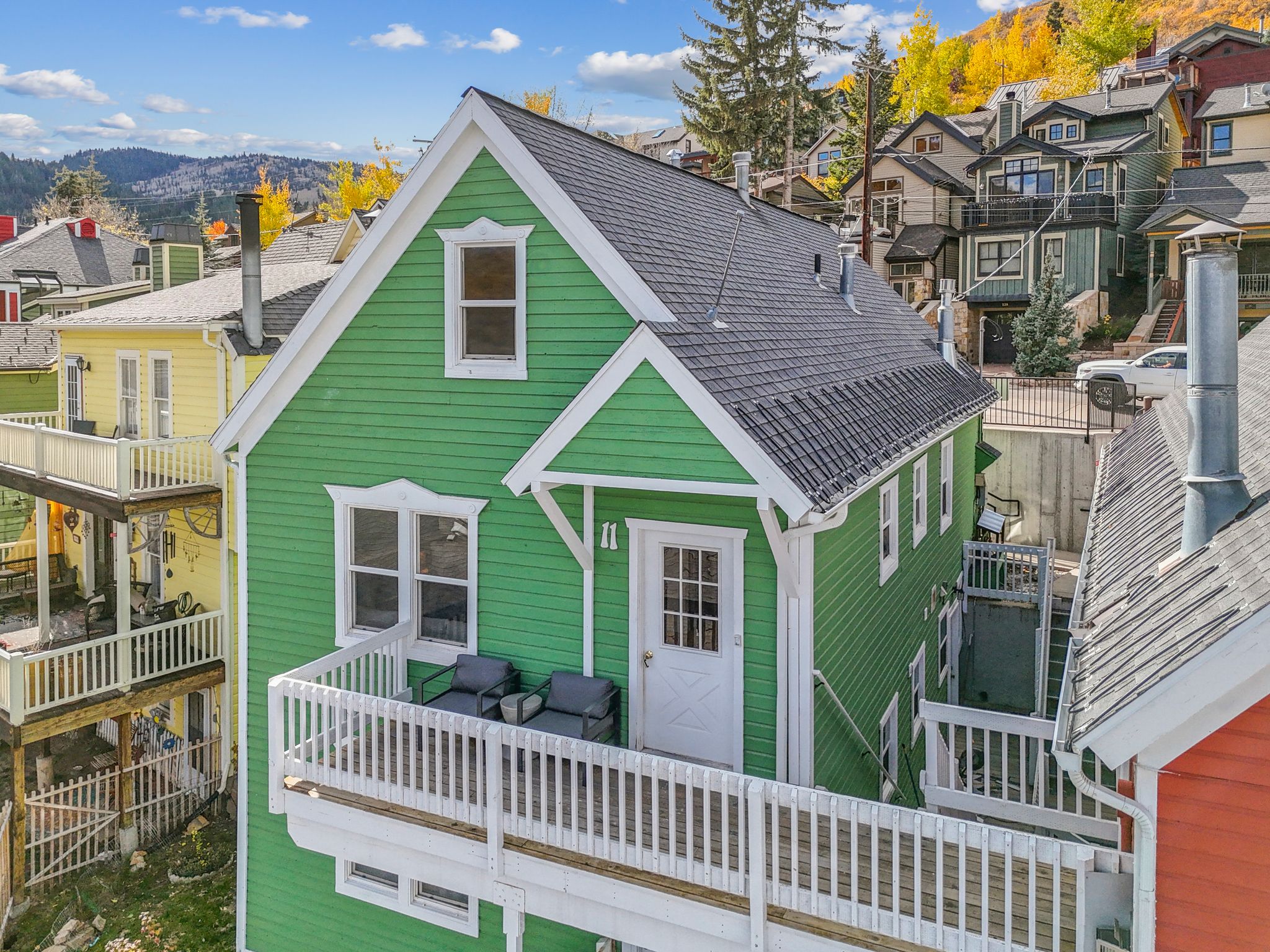 Green clapboard siding with white trim, featuring a dark shingle roof and a front balcony with white railings
