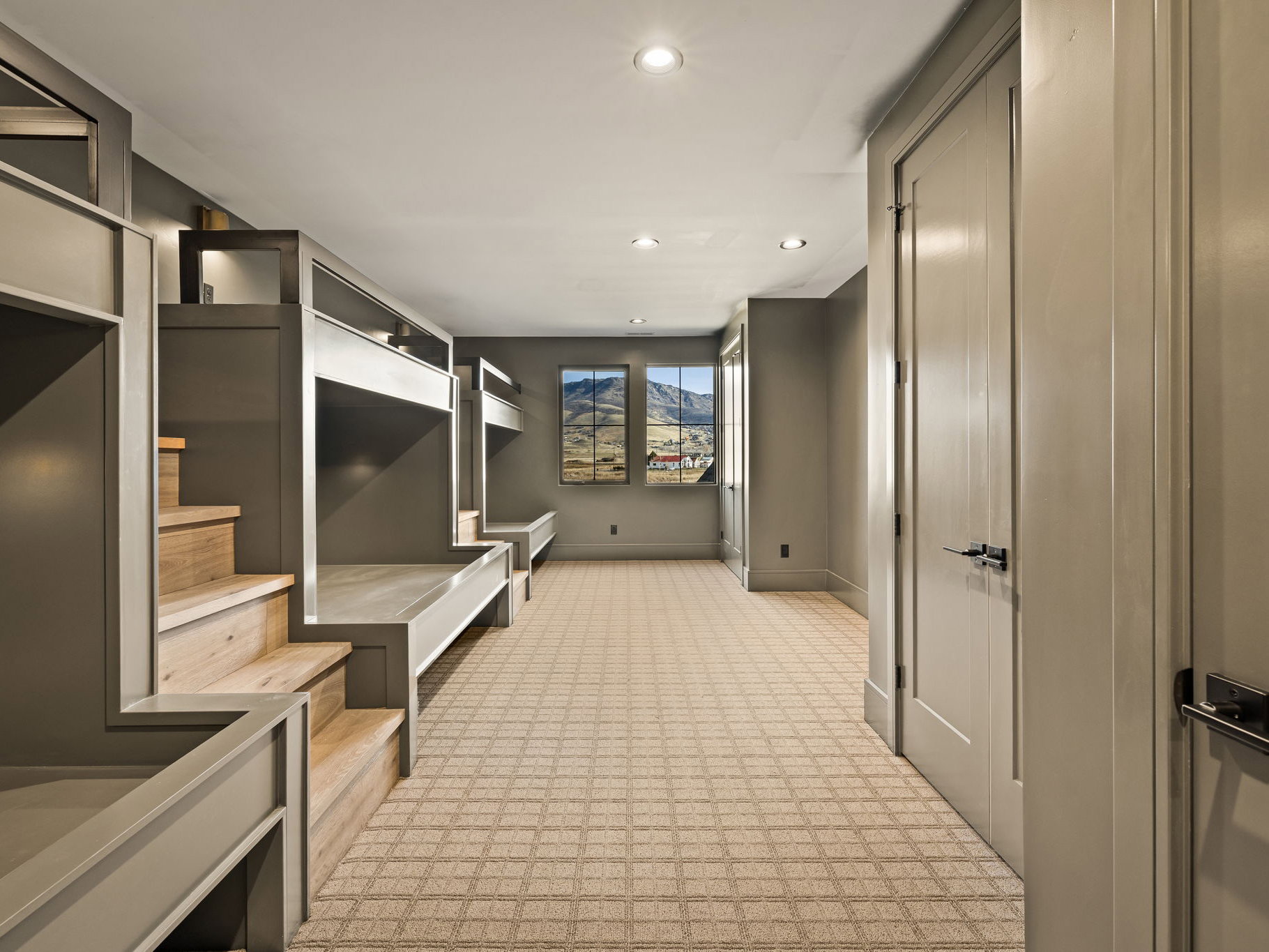 Built-in bunk beds with natural wood steps, recessed lighting, patterned carpeting, and multiple doors with dark hardware