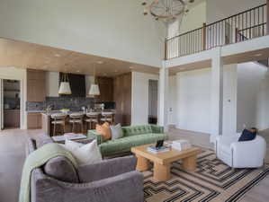 Open-concept living area featuring a double-height ceiling, light wood-finish flooring, a kitchen island with seating, a built-in range hood, and a second-story interior balcony with black metal railings