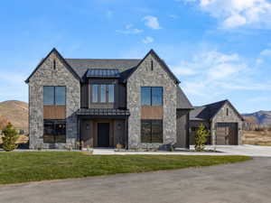 Modern stone and wood-clad exterior with multiple gables, large windows, an attached garage, and a paved driveway