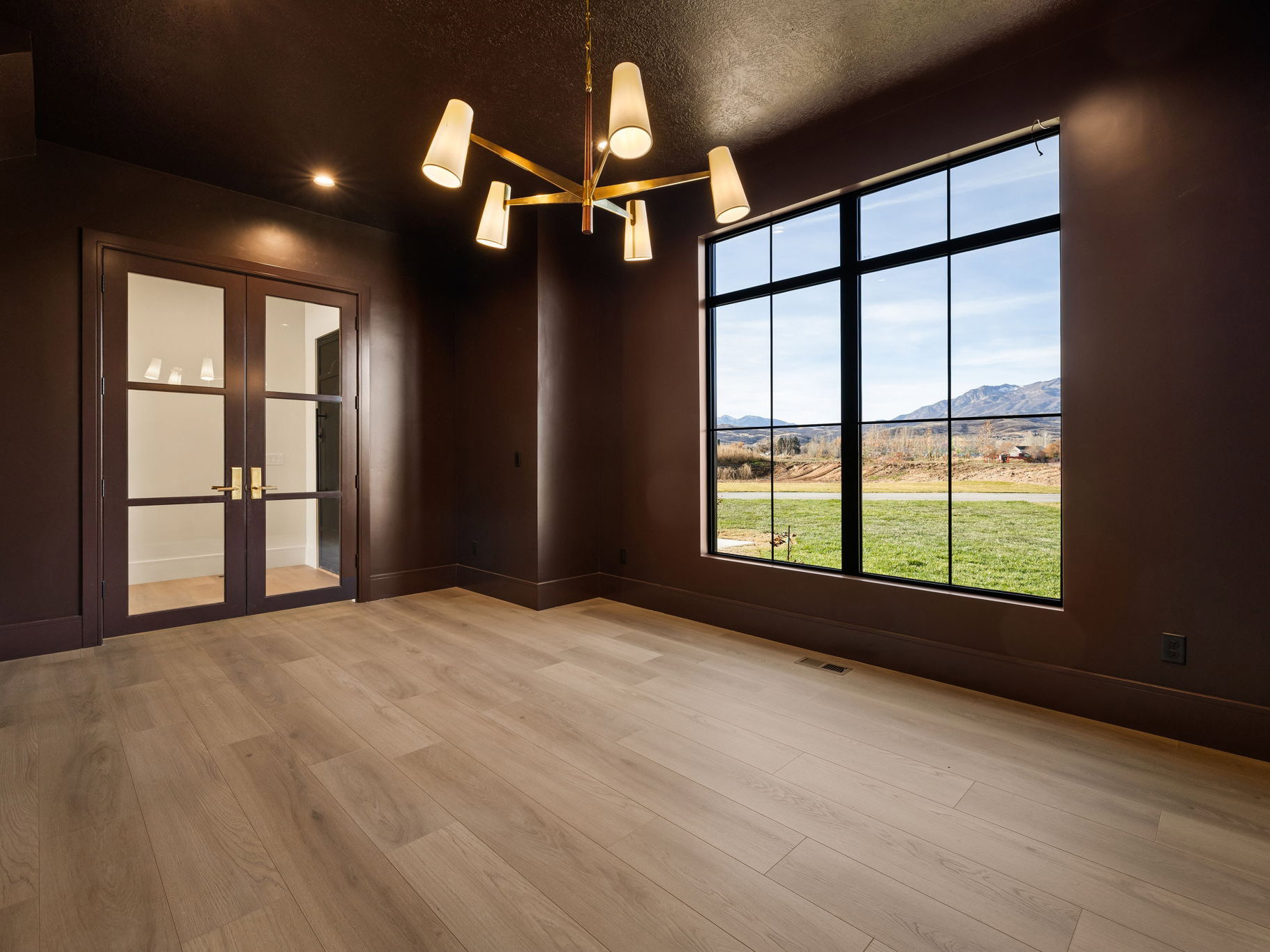 Room featuring a large picture window with mountain scenery, light wood-finish flooring, and dark walls