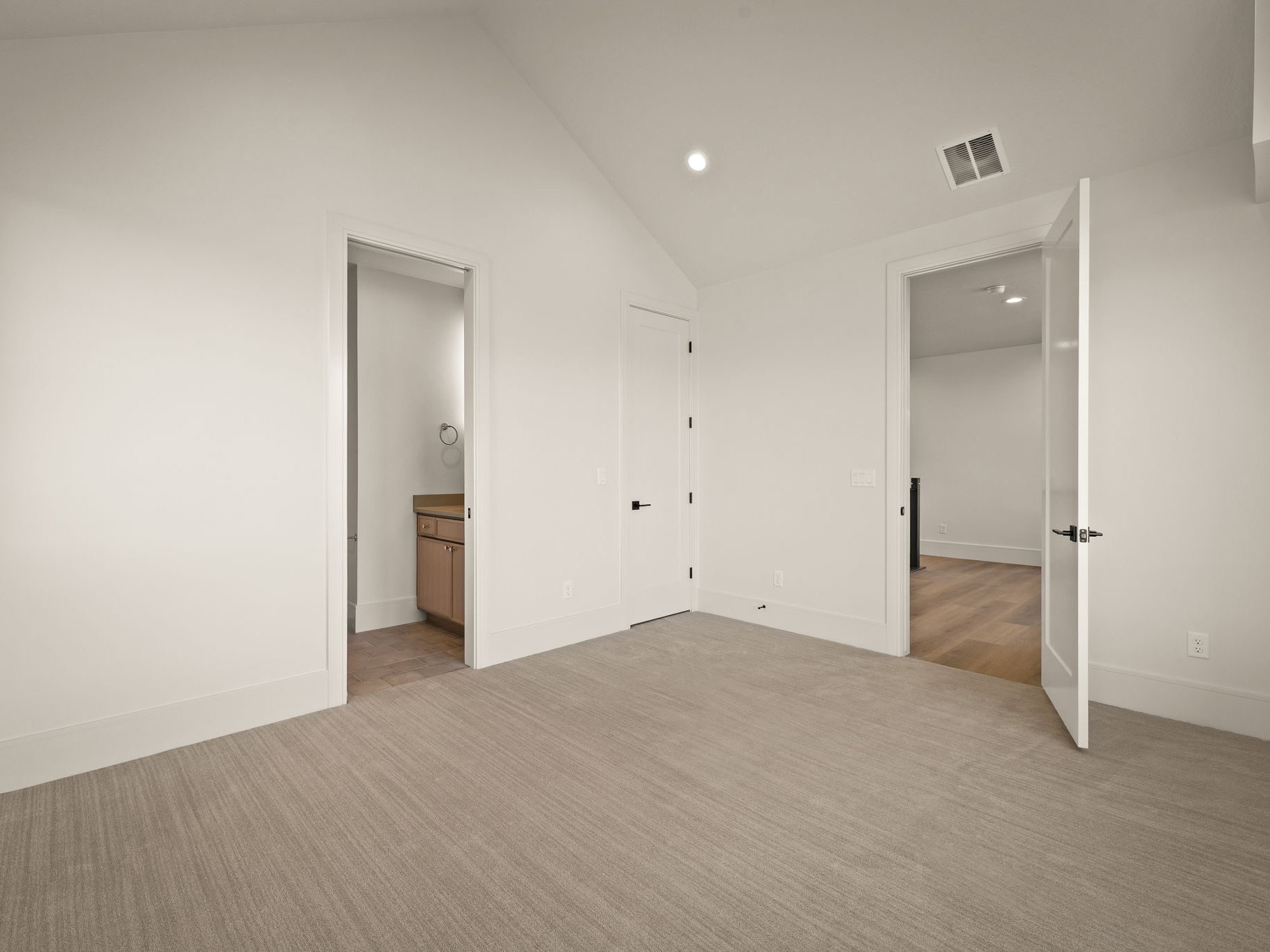 Spacious room featuring vaulted ceilings, recessed lighting, and light-toned patterned carpeting