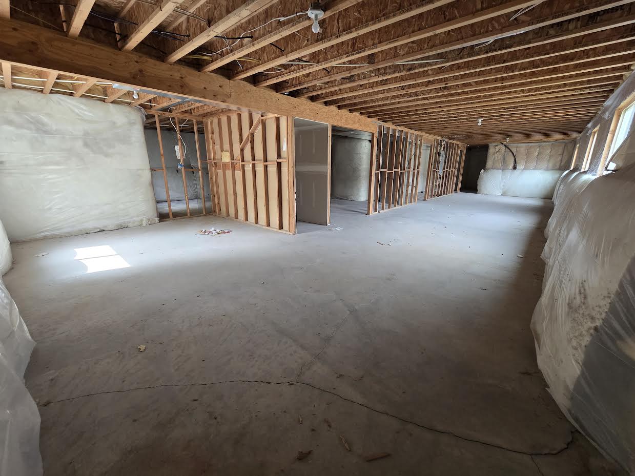 Spacious unfinished basement featuring exposed ceiling joists, framed interior walls, concrete flooring, and multiple window openings with insulation