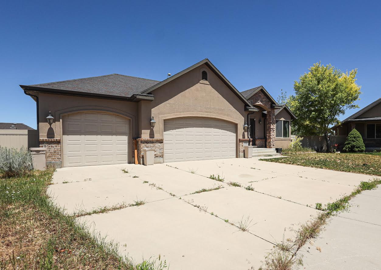 Stucco exterior with stone accents, featuring a multi-car garage with arched entrances, a covered entryway, and a stone-clad porch