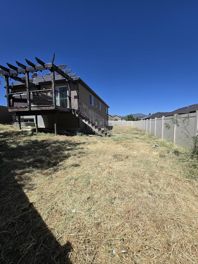 Expansive backyard featuring a multi-level wood deck with pergola, lower-level stairs, and a vinyl privacy fence