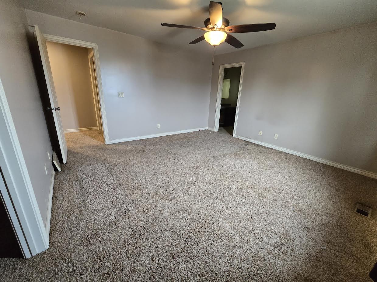 Spacious room featuring neutral carpeting, light-toned walls, and a ceiling fan with integrated lighting