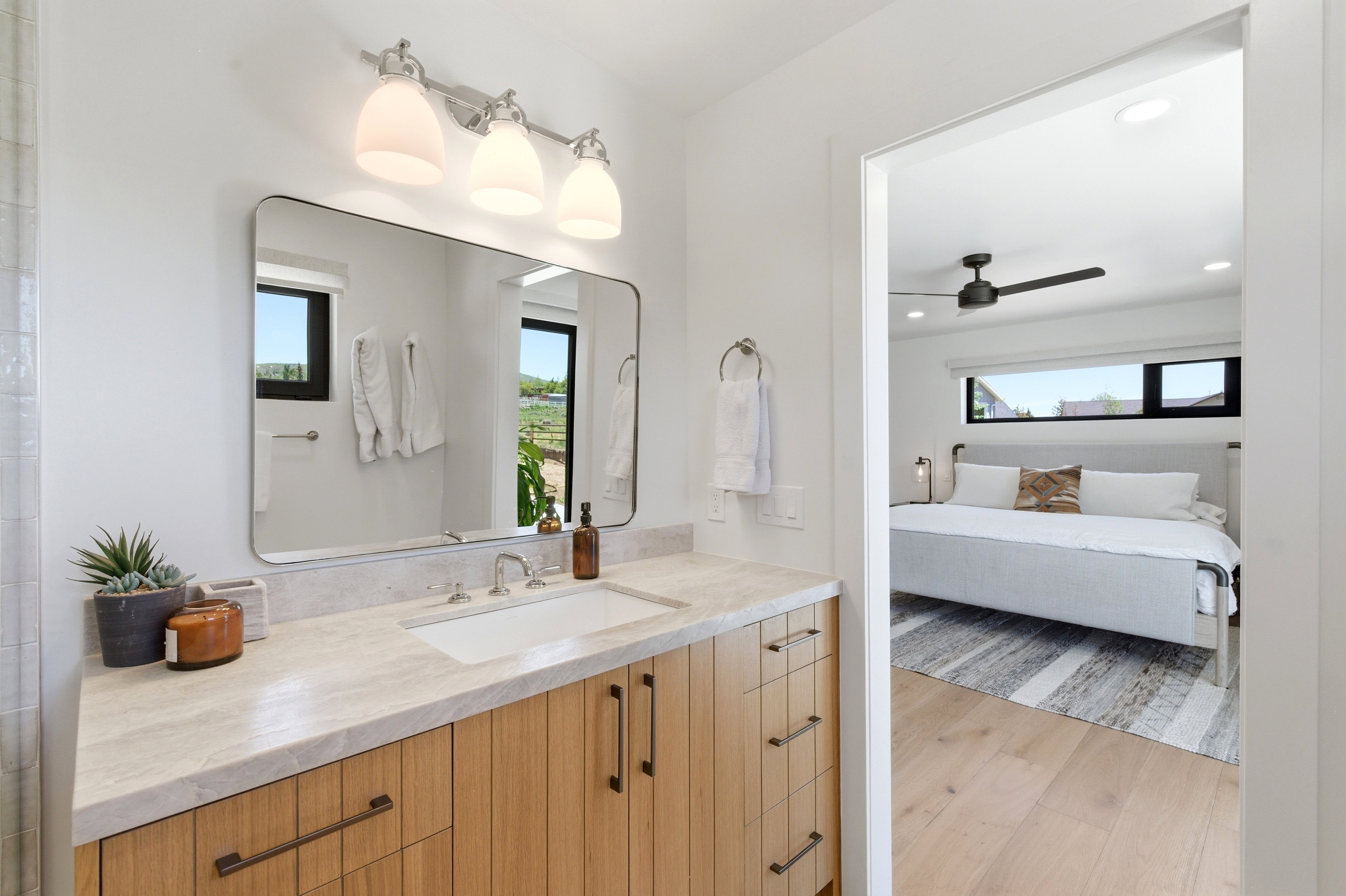Contemporary vanity featuring a light-toned countertop, undermount sink, and wood-finish cabinetry with dark hardware