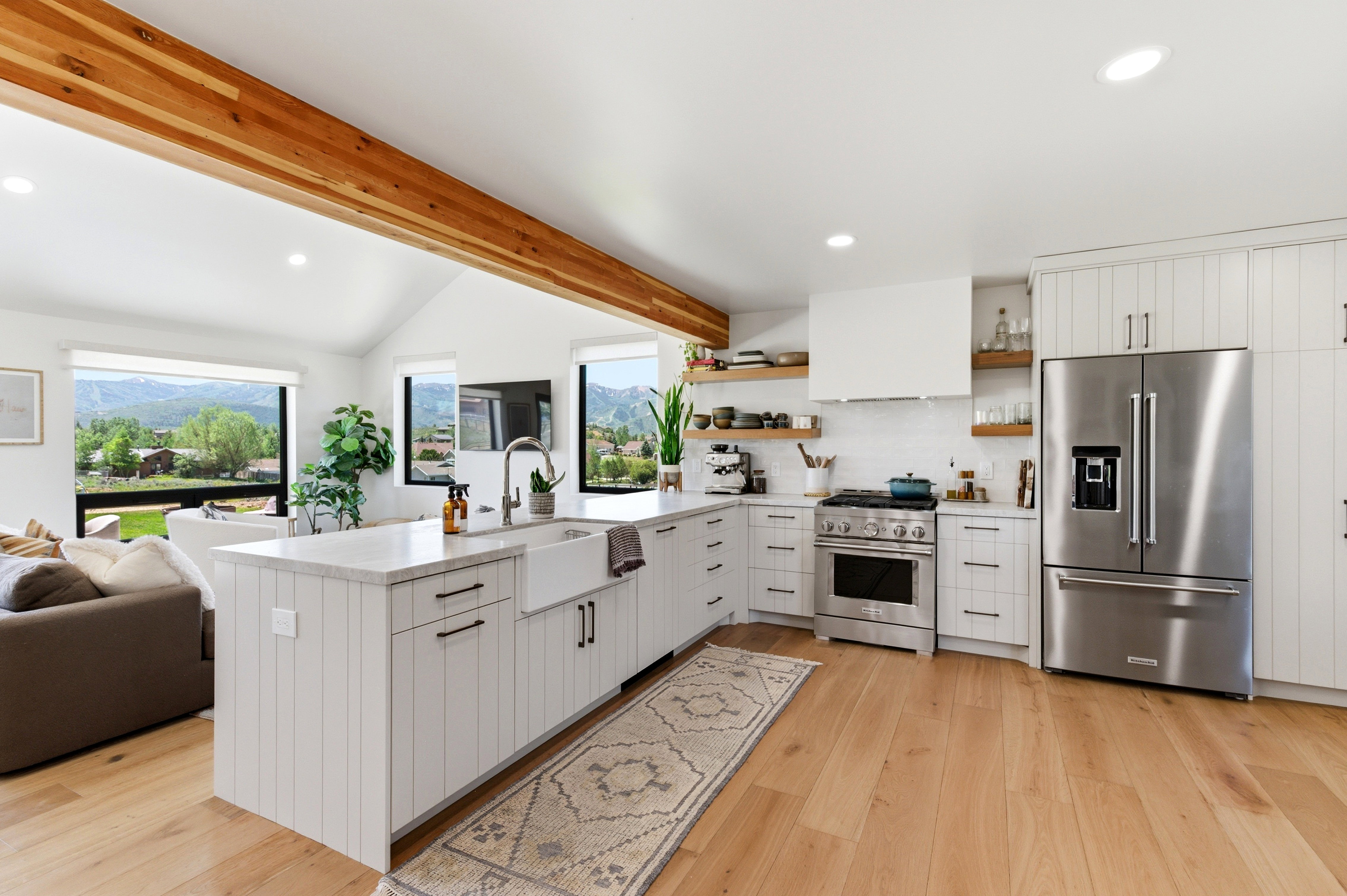 Modern kitchen featuring a large island with farmhouse sink, stainless steel appliances, open shelving, and wood-finish flooring