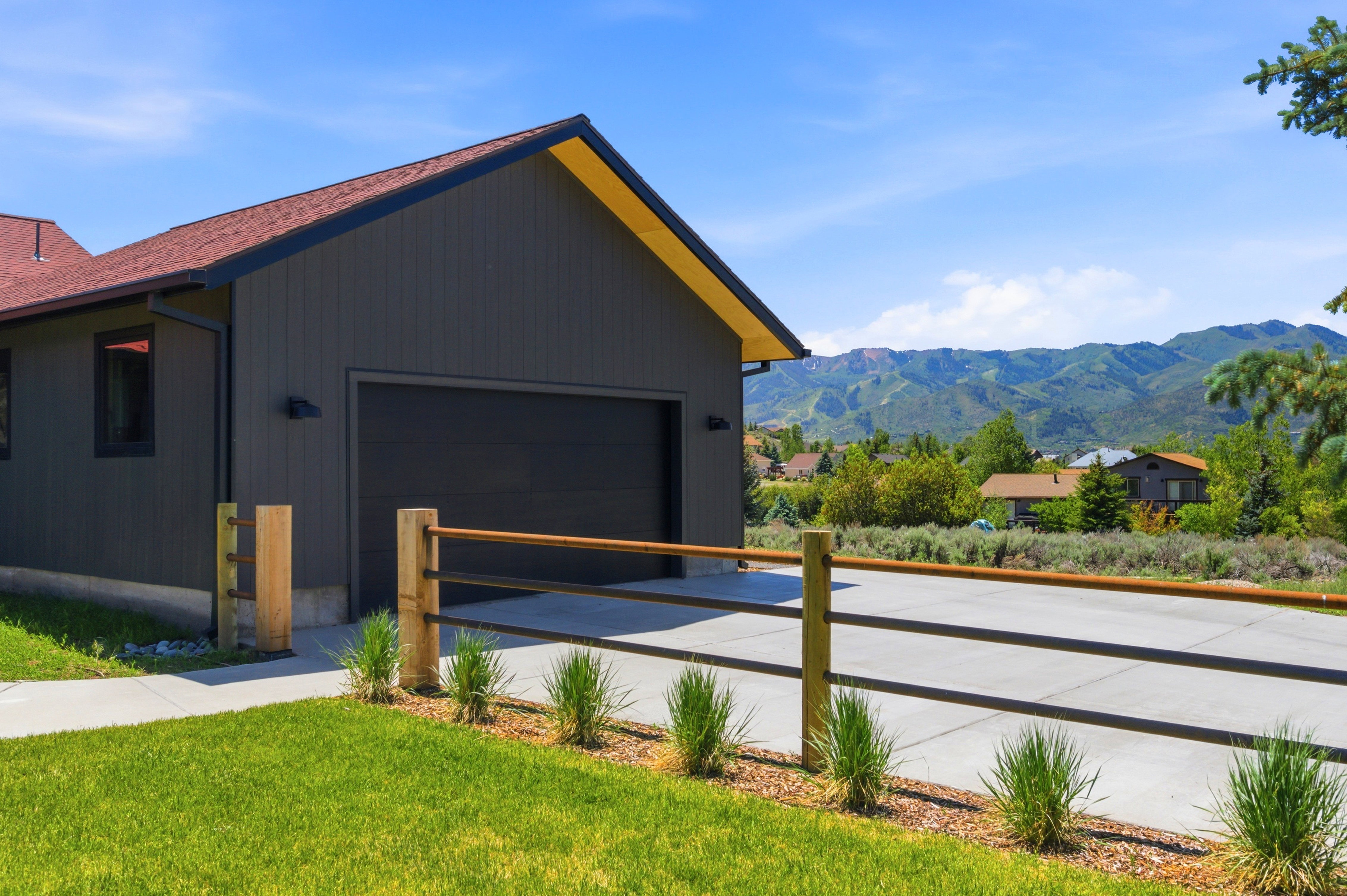 Modern exterior featuring dark vertical siding, a red shingle roof, and a prominent black garage door