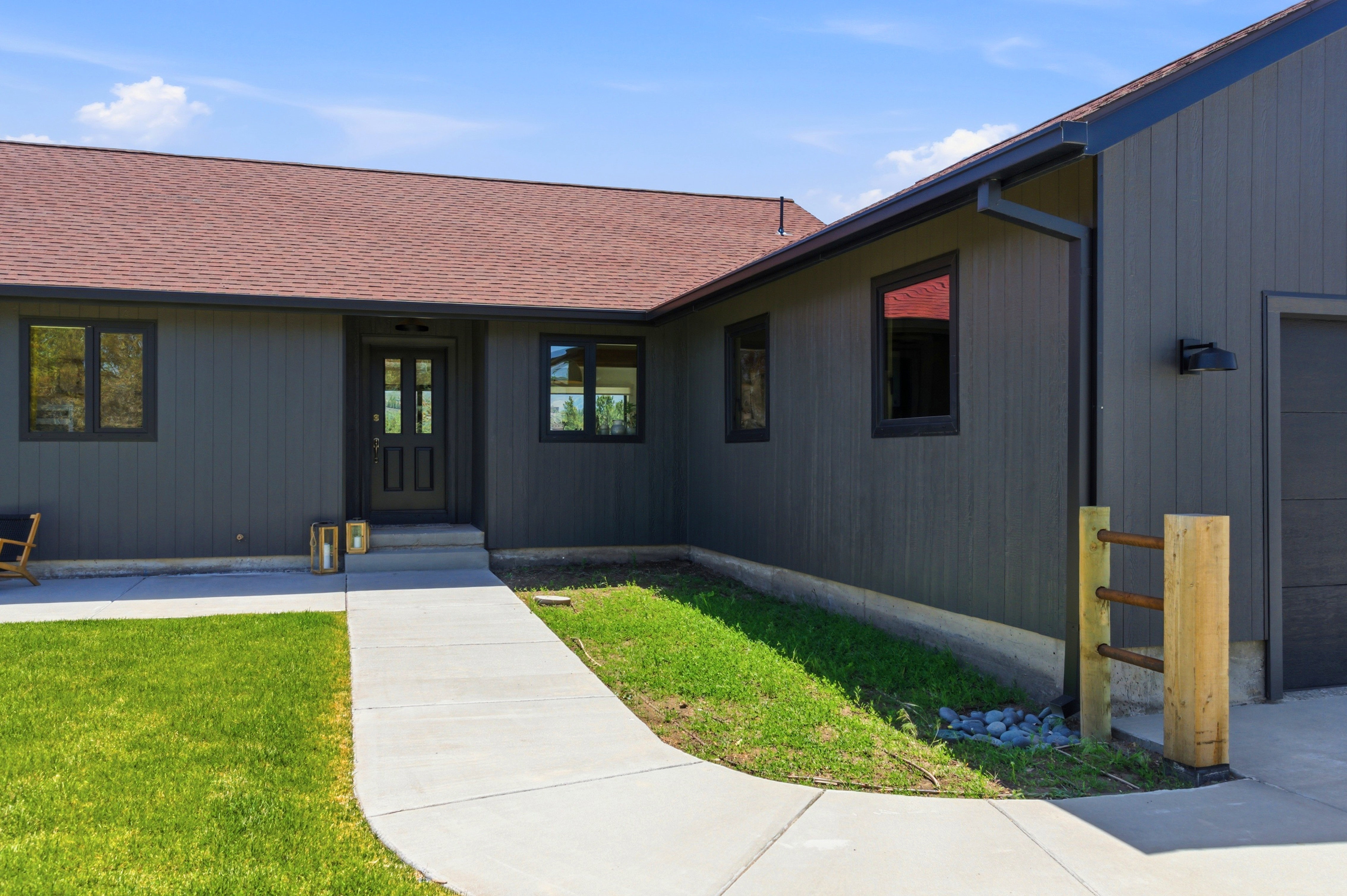 Exterior featuring dark gray vertical siding, a red shingle roof, and black window frames