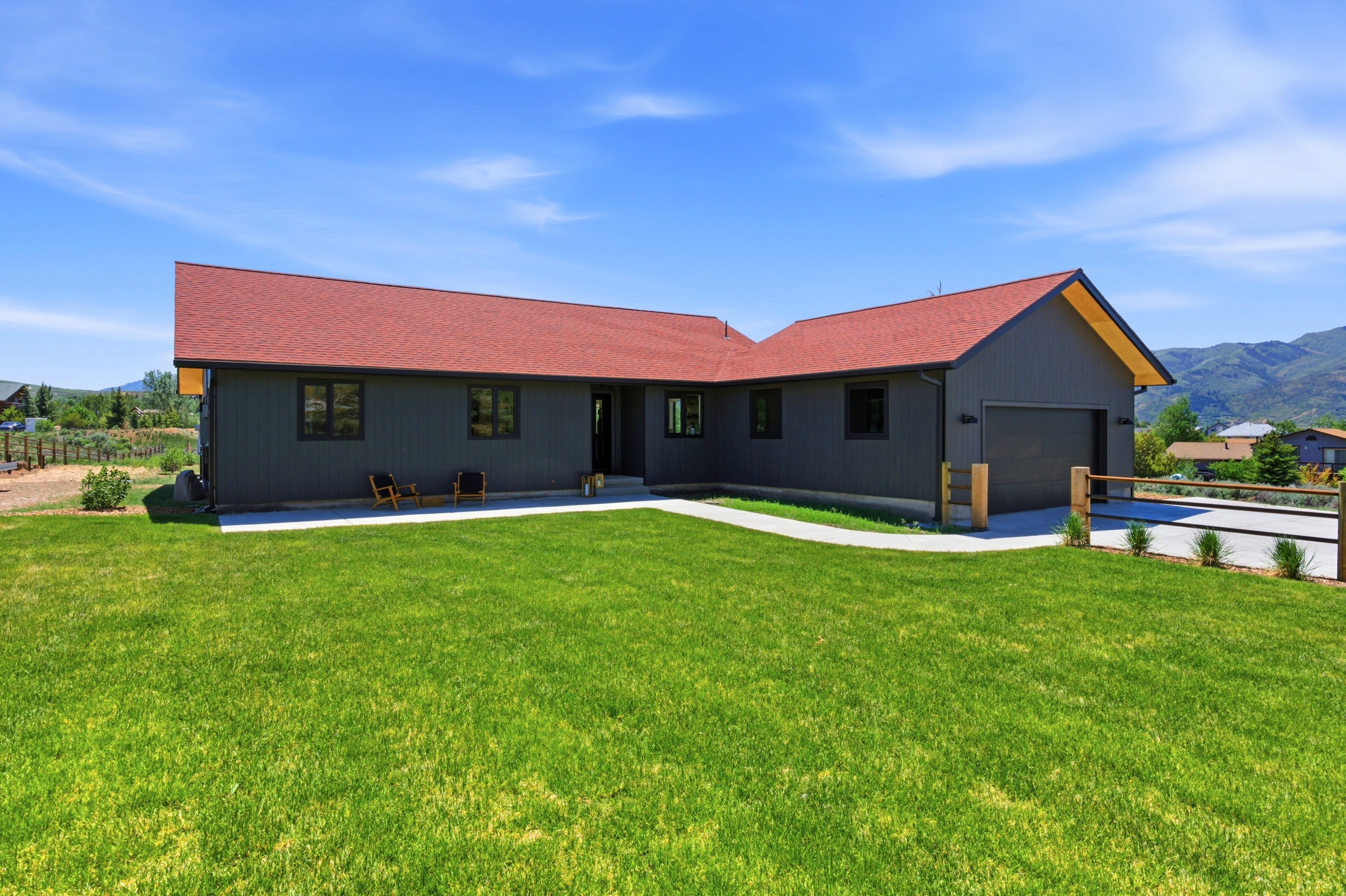 Contemporary exterior featuring dark gray vertical siding, a striking red roof, and a two-car garage with a matching dark gray door
