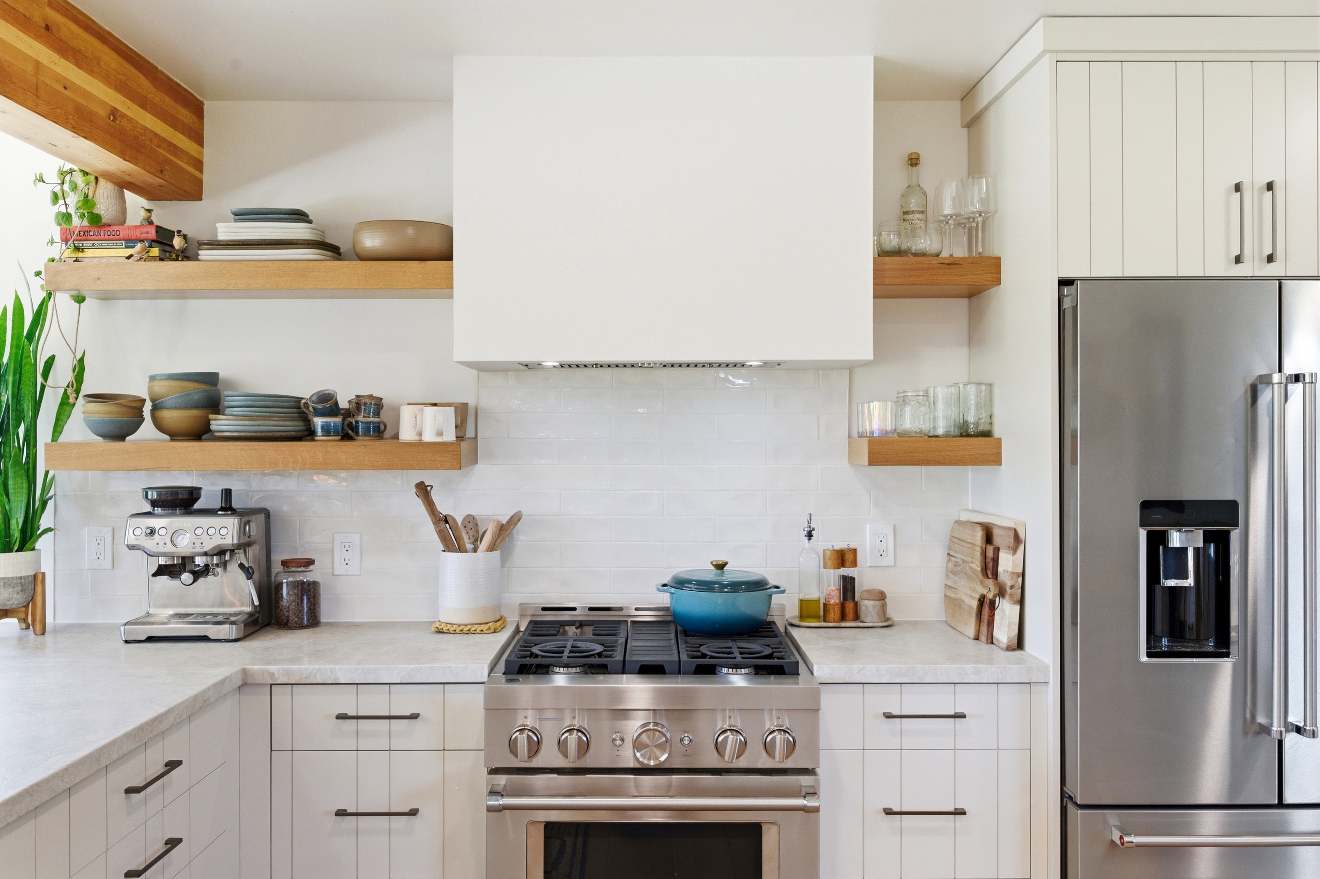 Modern kitchen featuring stainless steel appliances, open wood shelving, a white range hood, and light-toned countertops