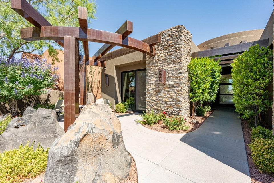 Exterior entry featuring a paved walkway, stone-clad walls, and a wooden pergola structure