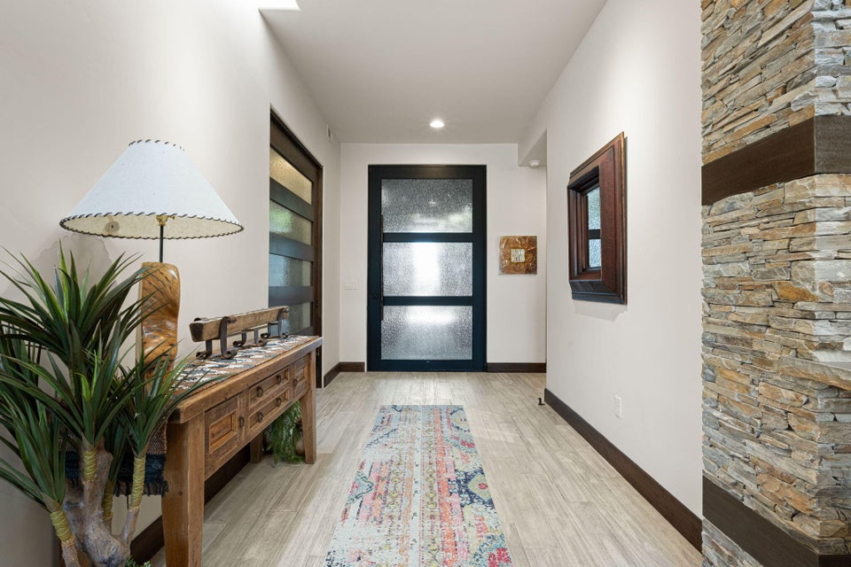 Entryway featuring a stacked stone accent wall with wood beam details, light wood-finish flooring, and a modern black entry door with frosted glass panels