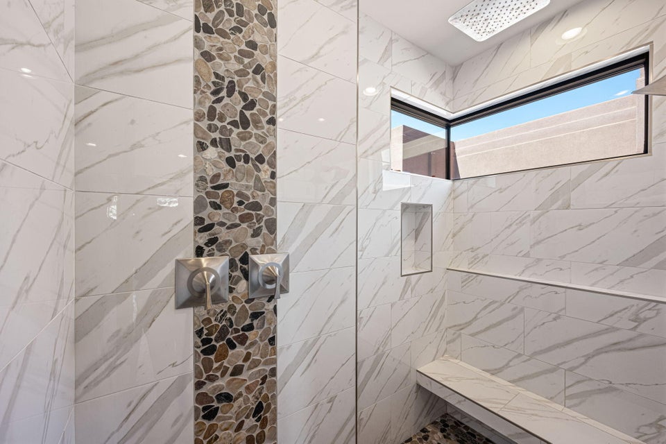 Walk-in shower with natural stone pebble accent tile, large format marble-look wall tile, a built-in bench, and a rectangular transom window