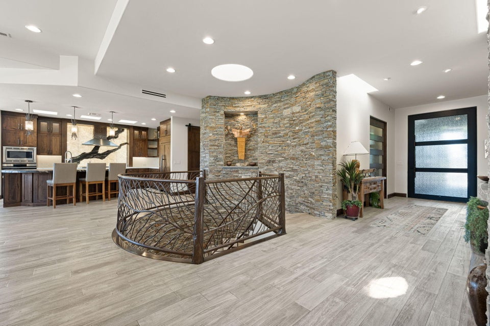 Open-concept living space featuring wood-finish flooring, a custom-designed metal staircase railing, a stacked stone accent wall with built-in niche, a skylight, and a kitchen with dark wood cabinetry