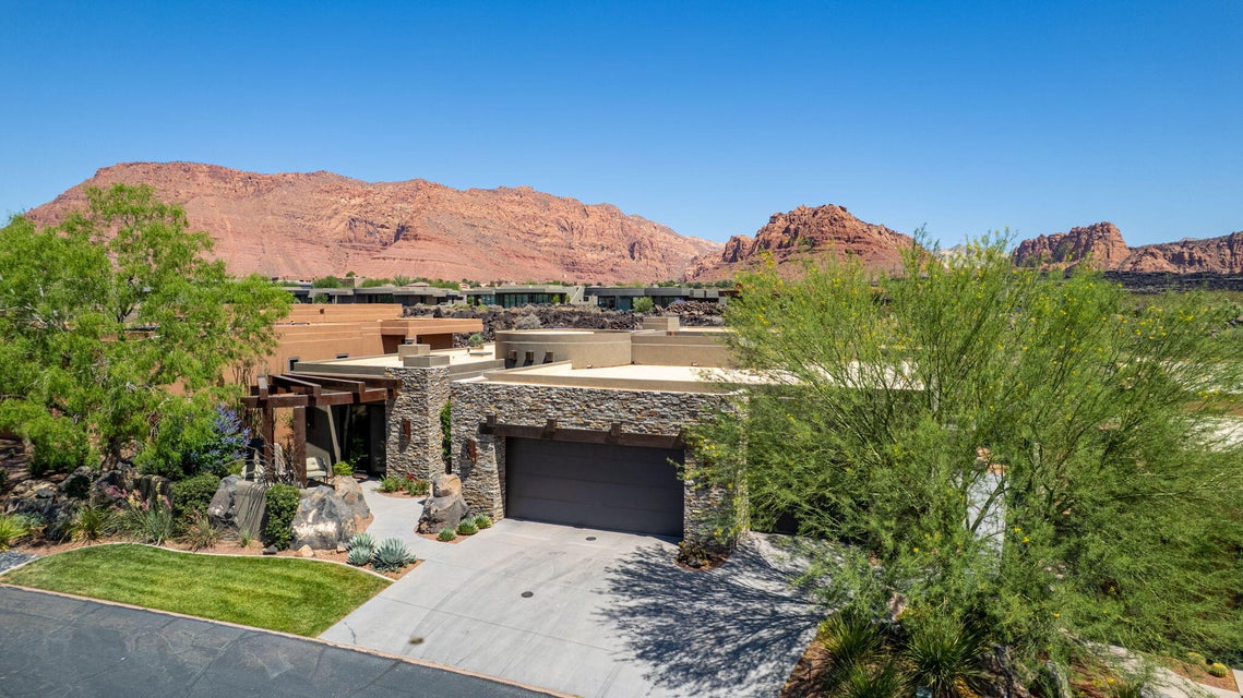 Modern desert-style residence with a stone facade, integrated garage, and a lush, rock-accented landscape