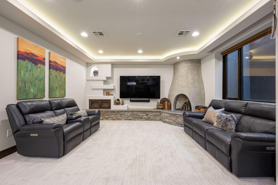 Living area with tray ceiling featuring recessed lighting and cove lighting, a built-in entertainment center with a stone-clad base, and a kiva-style fireplace